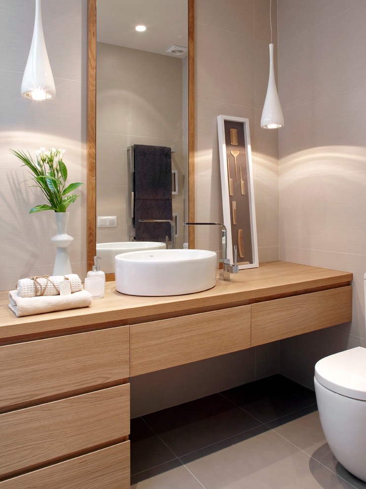 Mittelgroße Moderne Gästetoilette mit flächenbündigen Schrankfronten, Toilette mit Aufsatzspülkasten, grauer Wandfarbe, Keramikboden, Aufsatzwaschbecken, Waschtisch aus Holz, grauen Fliesen, hellen Holzschränken und brauner Waschtischplatte in Barcelona