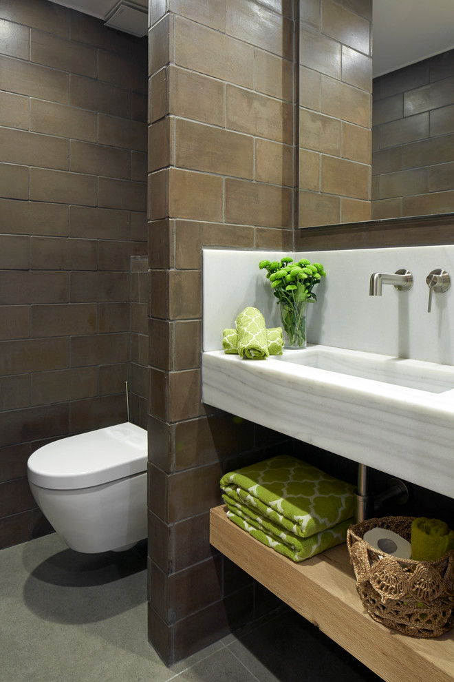 Ispirazione per un bagno di servizio design con nessun'anta, ante in legno chiaro, WC sospeso, piastrelle marroni, lavabo integrato e pavimento grigio