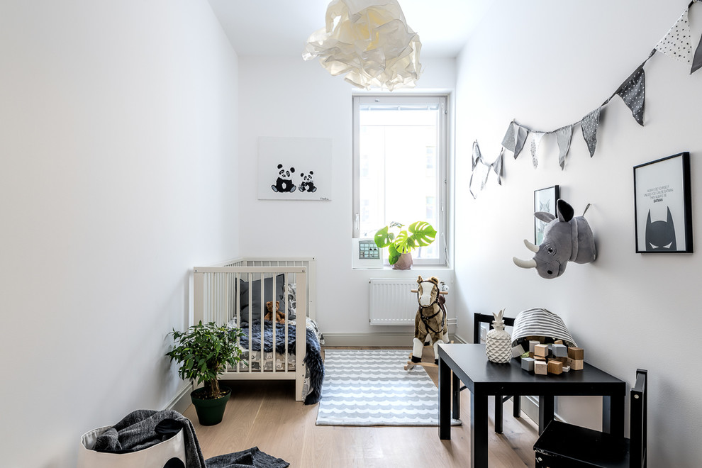 Bild på ett mellanstort minimalistiskt könsneutralt babyrum, med vita väggar, ljust trägolv och beiget golv