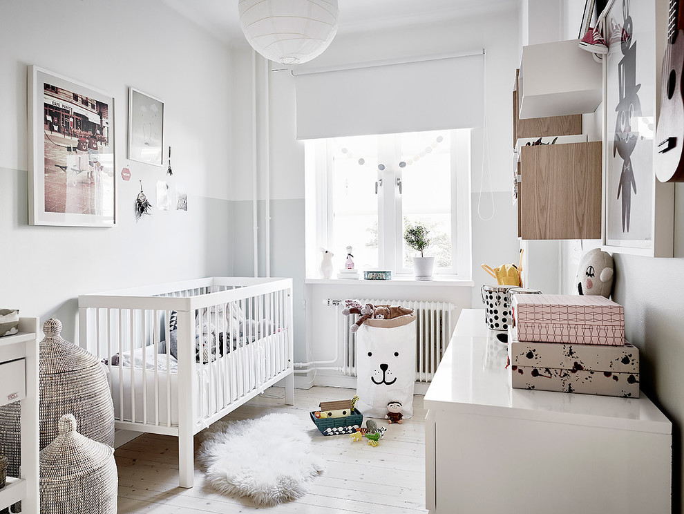Ejemplo de habitación de bebé neutra nórdica grande con paredes blancas, suelo de madera clara y suelo blanco