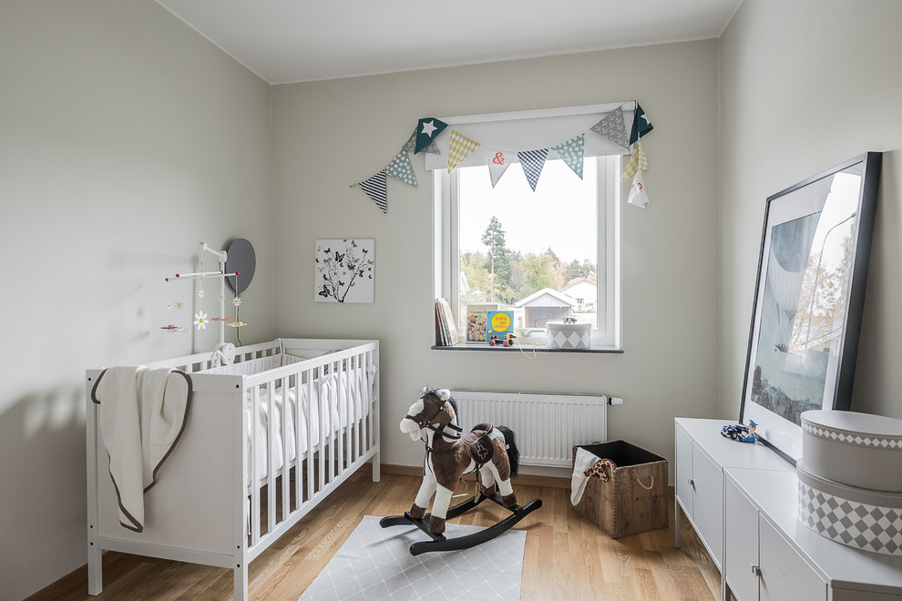 Design ideas for a medium sized scandinavian gender neutral nursery in Stockholm with beige walls, light hardwood flooring and beige floors.