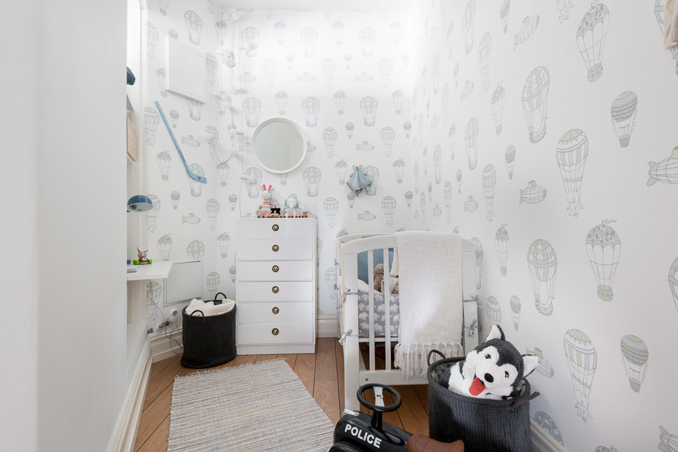 Immagine di una piccola cameretta per neonato scandinava con pareti bianche e pavimento in legno massello medio