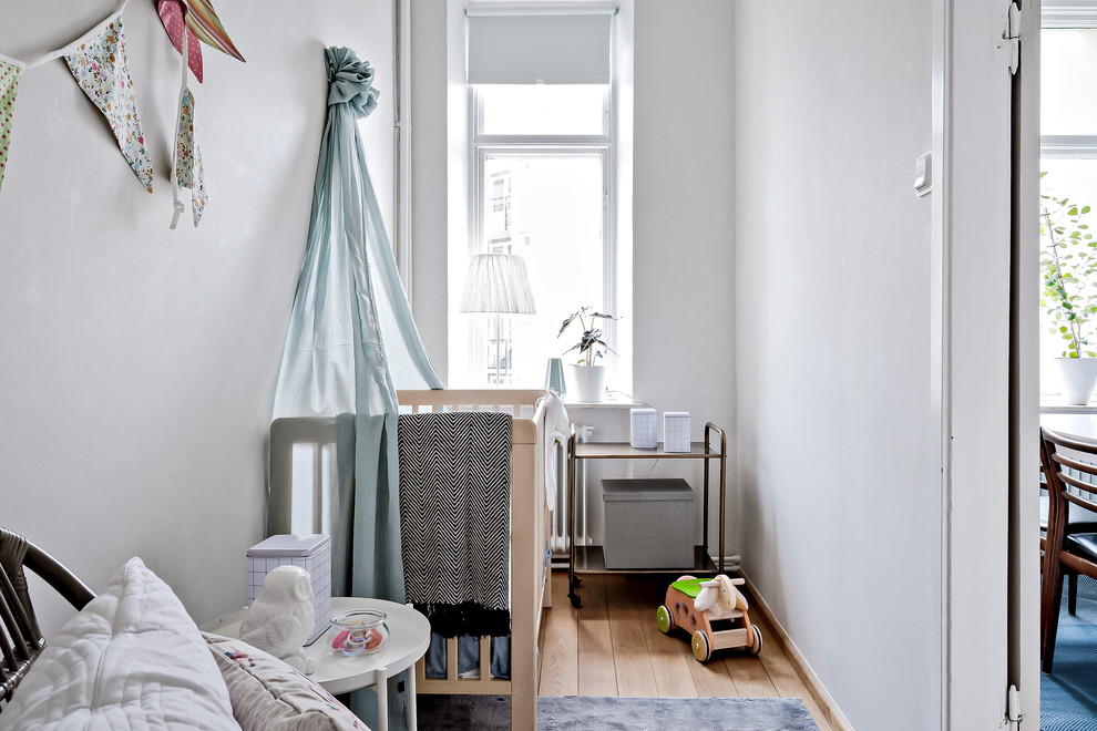 Modelo de habitación de bebé neutra escandinava pequeña con paredes blancas, suelo de madera clara y suelo beige