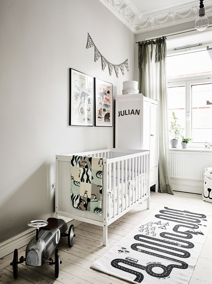 Bild på ett mellanstort skandinaviskt könsneutralt babyrum, med grå väggar, ljust trägolv och vitt golv