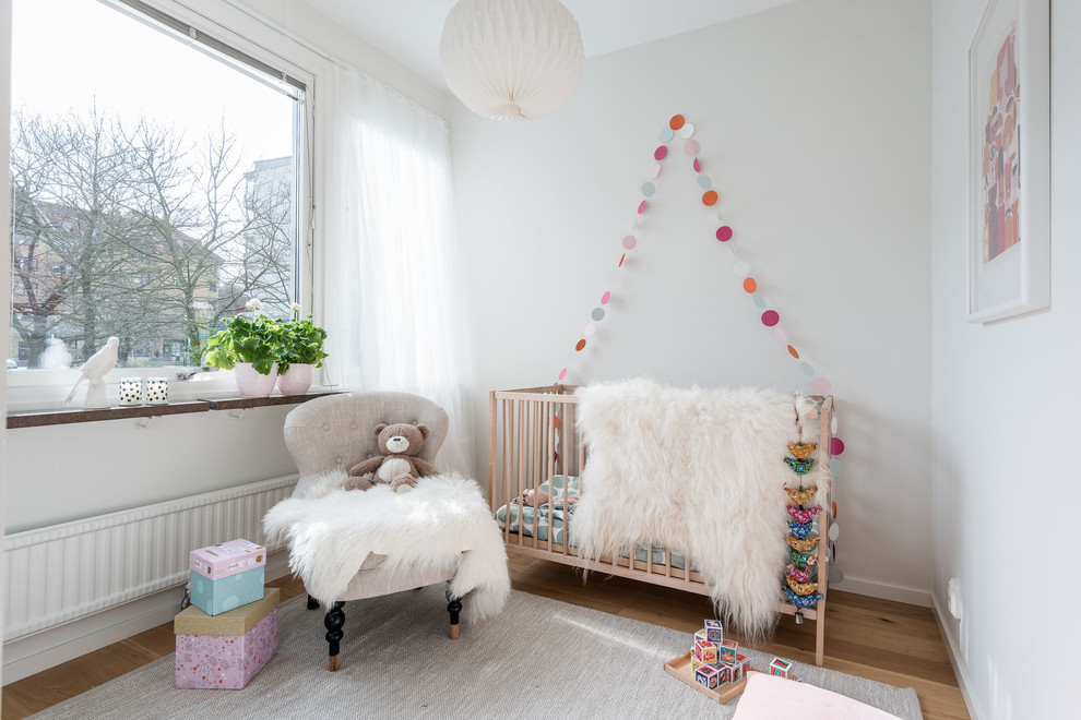 Idée de décoration pour une chambre de bébé neutre nordique de taille moyenne avec un mur blanc et parquet clair.