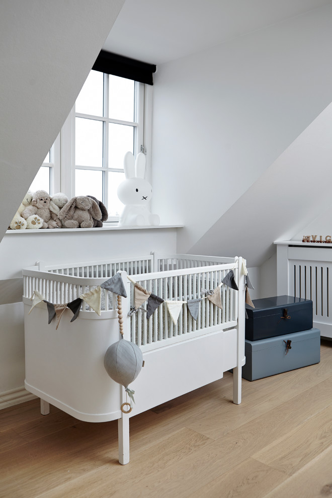 This is an example of a small scandinavian gender neutral nursery in Aarhus with white walls, light hardwood flooring and beige floors.