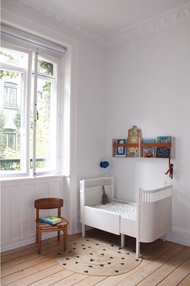 Foto di una cameretta per neonati neutra nordica di medie dimensioni con pareti bianche, pavimento in legno massello medio e pavimento marrone