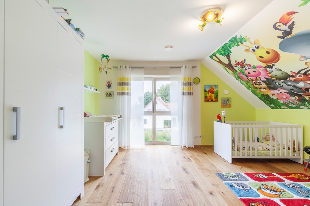 Modelo de habitación de bebé neutra actual grande con paredes verdes, suelo de madera en tonos medios y suelo marrón