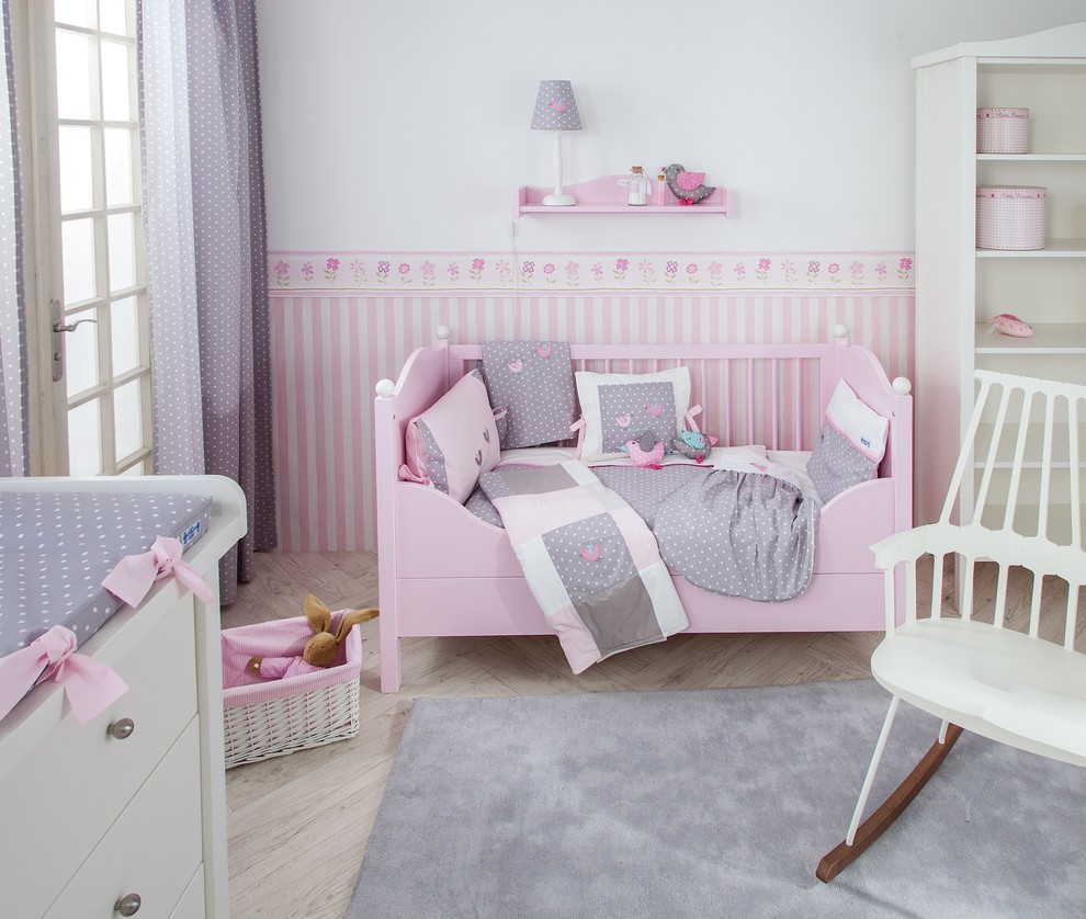 This is an example of a traditional nursery for girls in Munich with pink walls, light hardwood flooring and beige floors.