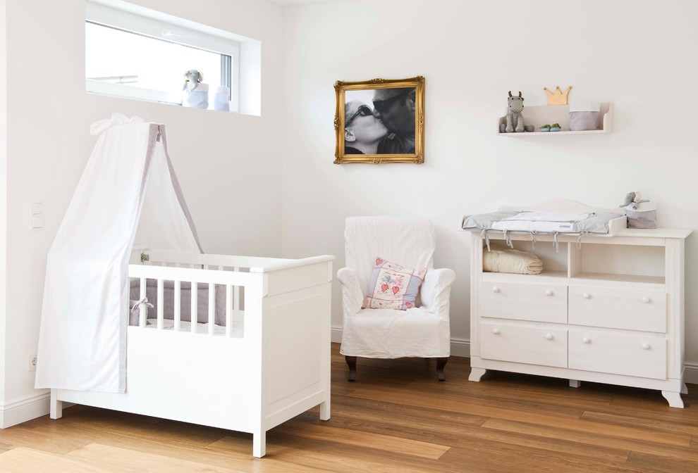 Idée de décoration pour une chambre de bébé neutre tradition de taille moyenne avec un mur blanc, un sol en bois brun et un sol marron.