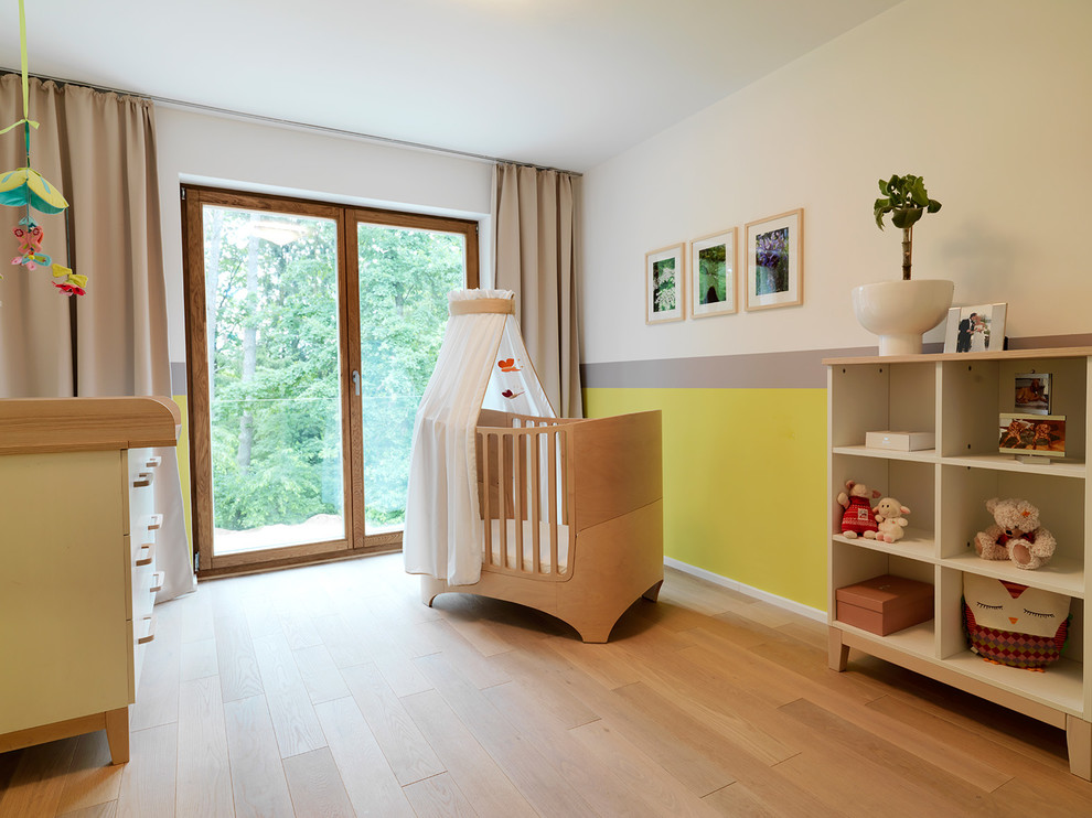 Réalisation d'une chambre de bébé neutre design de taille moyenne avec un mur jaune et un sol en bois brun.