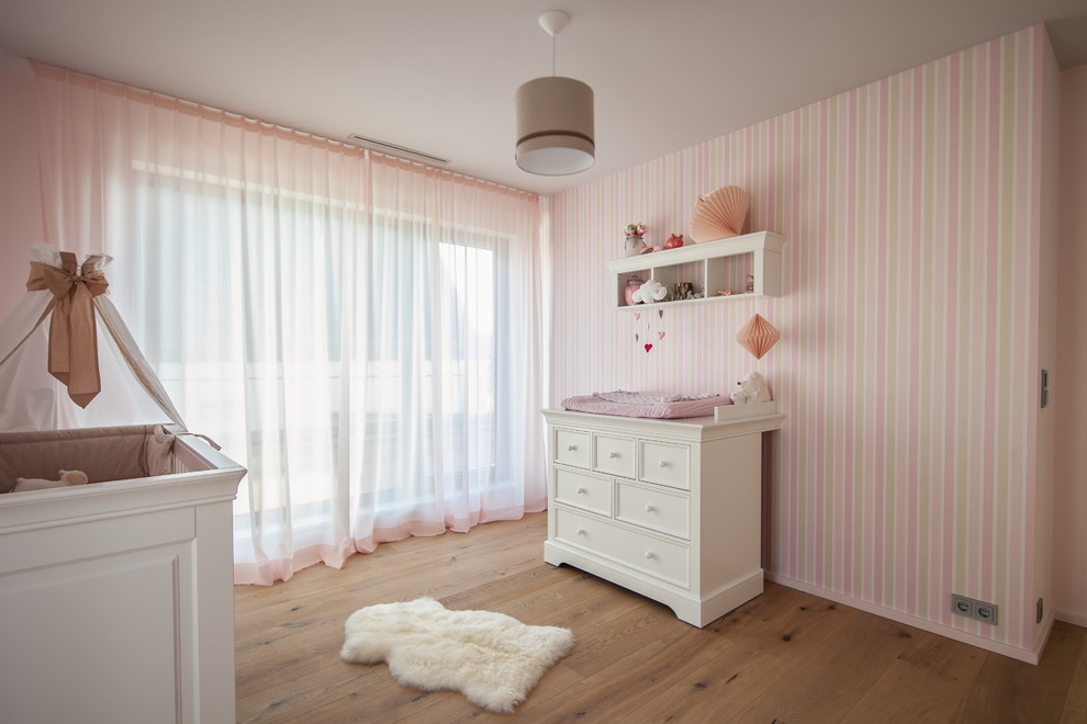 Medium sized contemporary nursery for girls in Munich with pink walls, light hardwood flooring and brown floors.