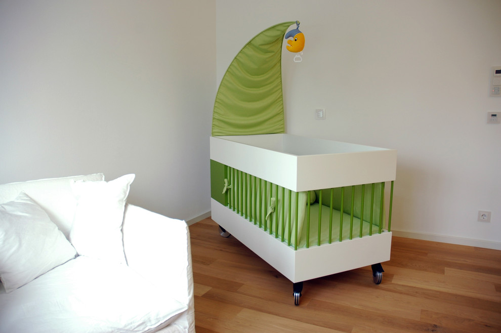 Idées déco pour une chambre de bébé neutre contemporaine de taille moyenne avec un mur blanc, un sol en bois brun et un sol marron.