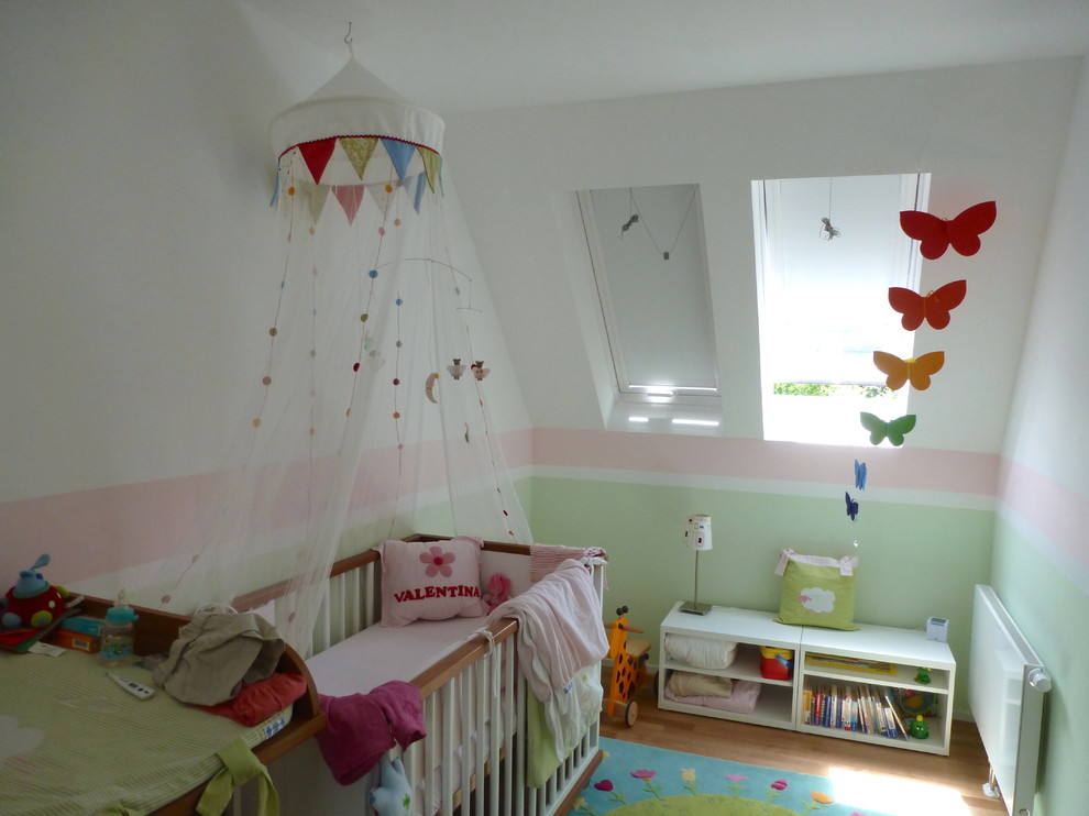 Imagen de habitación de bebé niña actual pequeña con suelo de madera clara