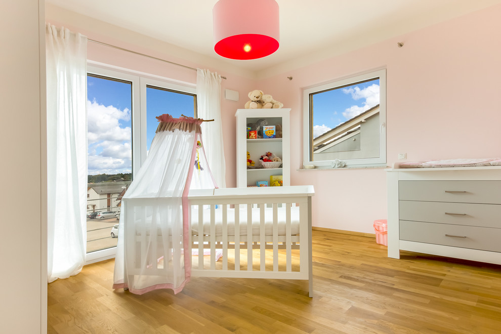 Kleines Modernes Babyzimmer mit rosa Wandfarbe und braunem Holzboden in Köln