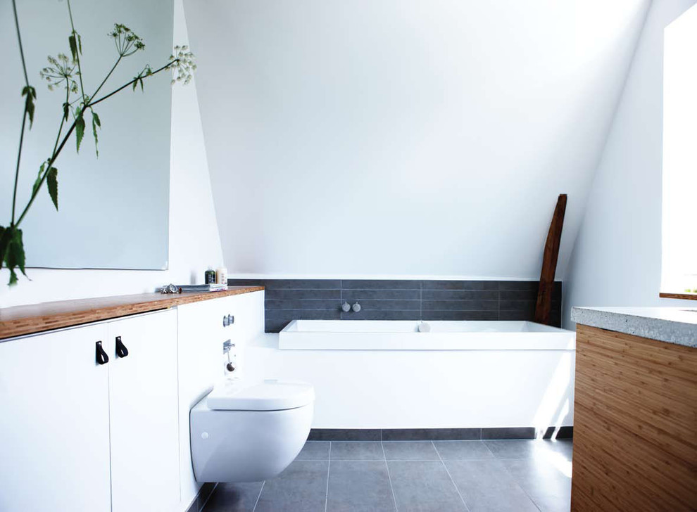 Inredning av ett skandinaviskt mellanstort en-suite badrum, med vita skåp, ett platsbyggt badkar, en vägghängd toalettstol, grå kakel, vita väggar, släta luckor, stenkakel och klinkergolv i keramik