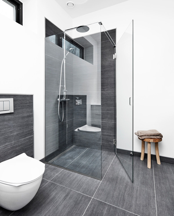 Inredning av ett nordiskt badrum, med en vägghängd toalettstol, flerfärgad kakel, flerfärgade väggar, grått golv och dusch med gångjärnsdörr