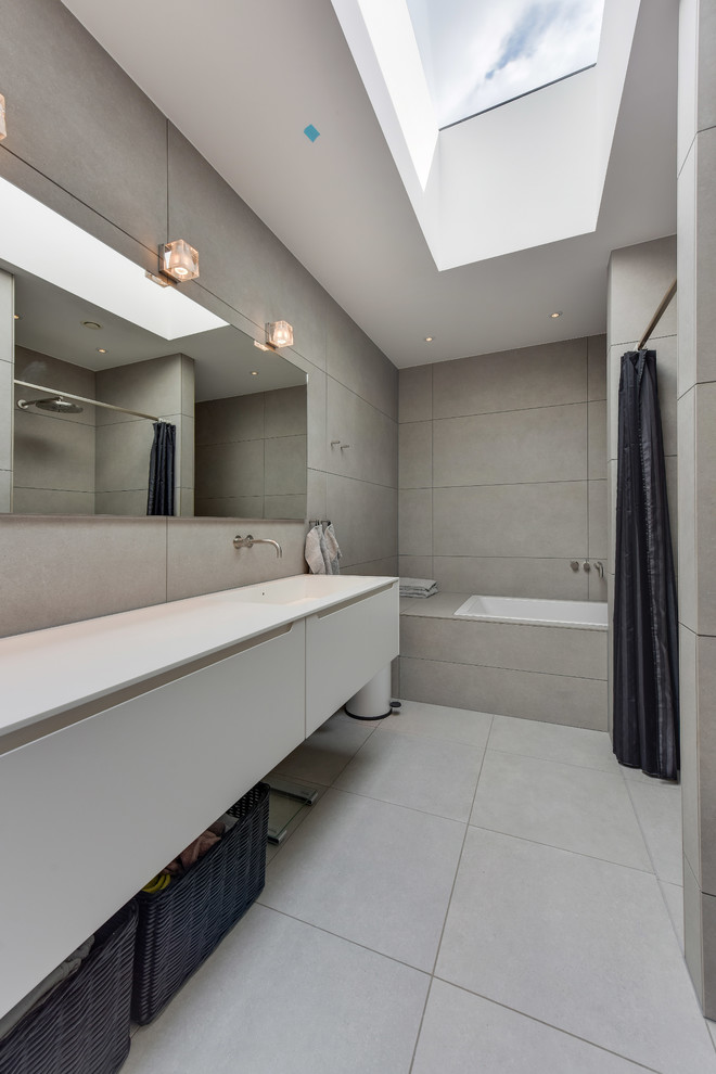 Cette image montre une salle de bain longue et étroite minimaliste avec un carrelage gris, un mur gris, un sol gris, une baignoire en alcôve et une grande vasque.