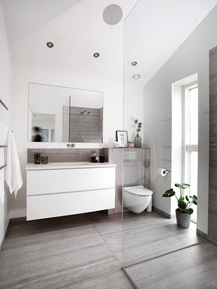 Ispirazione per una stanza da bagno contemporanea con ante lisce, ante bianche, doccia a filo pavimento, piastrelle grigie, pareti bianche, lavabo integrato, pavimento grigio e top bianco
