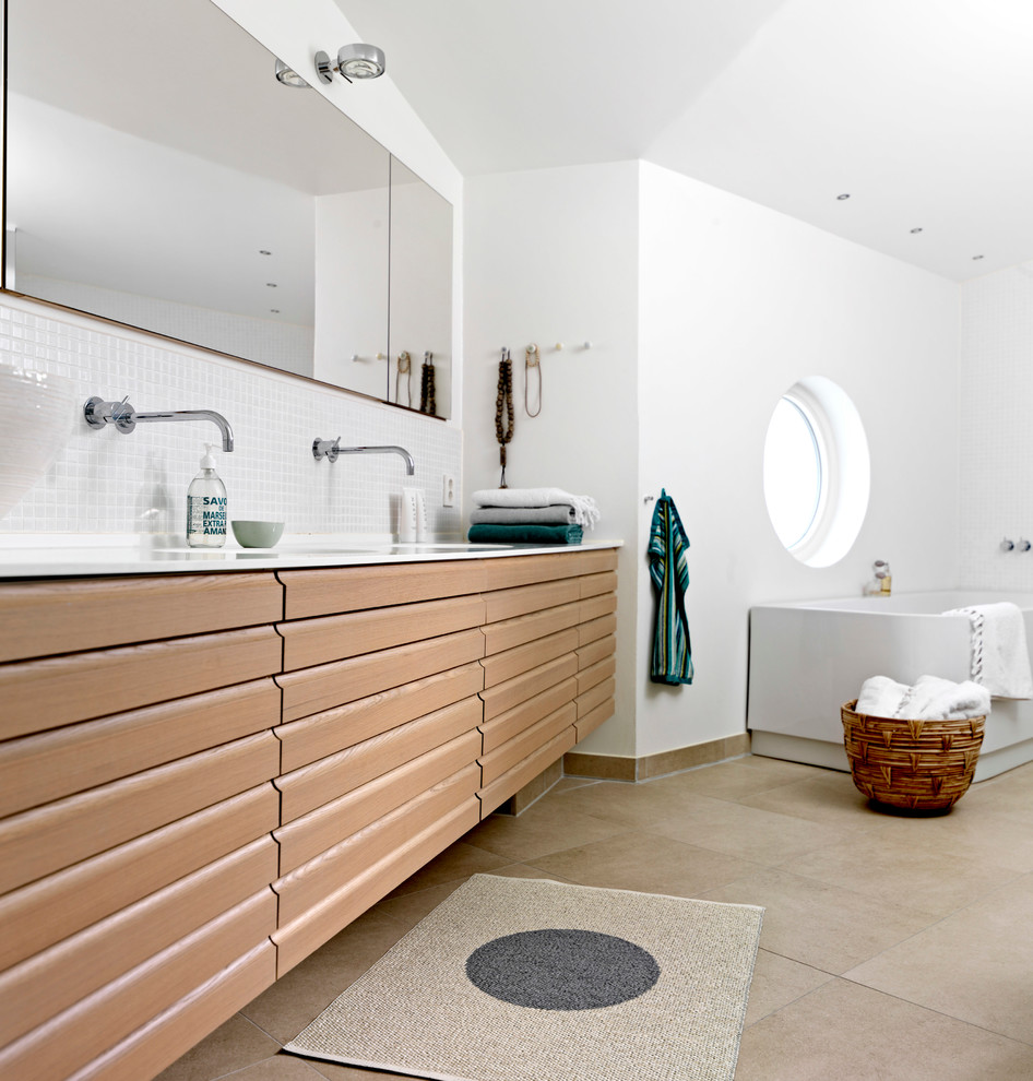 Réalisation d'une très grande salle de bain principale nordique en bois clair avec une baignoire encastrée, un carrelage gris, mosaïque, un mur blanc, un sol en carrelage de céramique, un lavabo intégré, un plan de toilette en stratifié et un placard à porte plane.