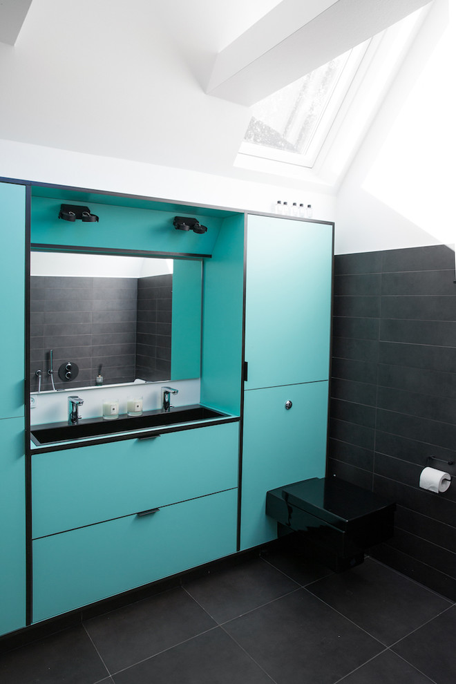 Example of a mid-sized trendy black floor bathroom design in Copenhagen with flat-panel cabinets, turquoise cabinets, a wall-mount toilet, black walls and a trough sink