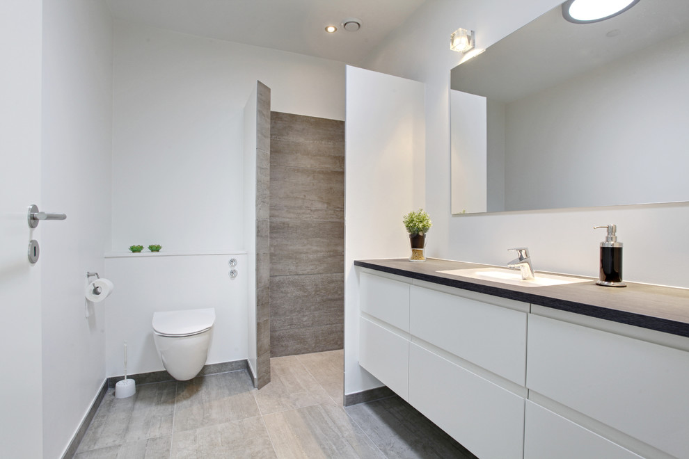 Inredning av ett modernt mellanstort en-suite badrum, med släta luckor, vita skåp, en öppen dusch, en vägghängd toalettstol, vita väggar, ett nedsänkt handfat, vit kakel, stenkakel, klinkergolv i keramik, granitbänkskiva och med dusch som är öppen