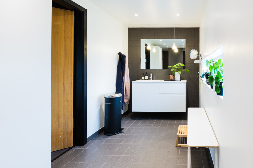 オーフスにある北欧スタイルのおしゃれな浴室 (フラットパネル扉のキャビネット、白いキャビネット、黒いタイル、白い壁、グレーの床、白い洗面カウンター) の写真