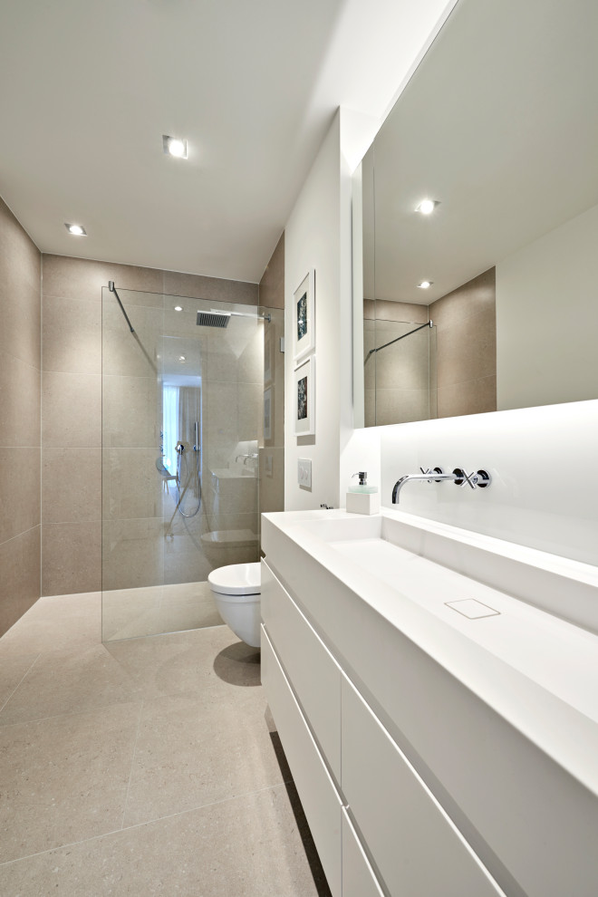 Inredning av ett modernt mellanstort en-suite badrum, med luckor med upphöjd panel, vita skåp, en kantlös dusch, stenkakel, vita väggar, cementgolv, beiget golv, beige kakel, ett nedsänkt handfat, bänkskiva i akrylsten, med dusch som är öppen och en vägghängd toalettstol