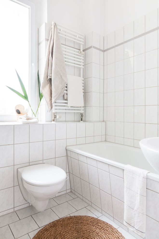 Kleines Skandinavisches Duschbad mit weißen Schränken, Eckbadewanne, weißen Fliesen, weißer Wandfarbe und Keramikboden in Berlin