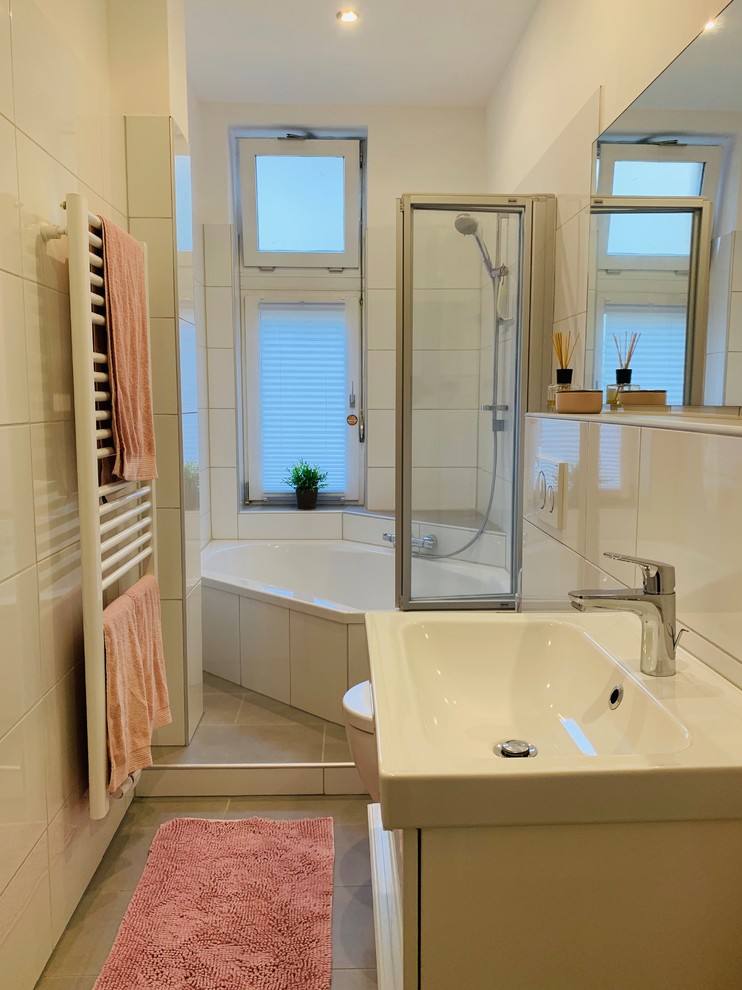 На фото: ванная комната среднего размера в современном стиле с белыми фасадами, угловой ванной, душем над ванной, инсталляцией, белой плиткой, керамической плиткой, белыми стенами, полом из керамической плитки, душевой кабиной, подвесной раковиной, столешницей из искусственного камня, серым полом, душем с распашными дверями и белой столешницей с