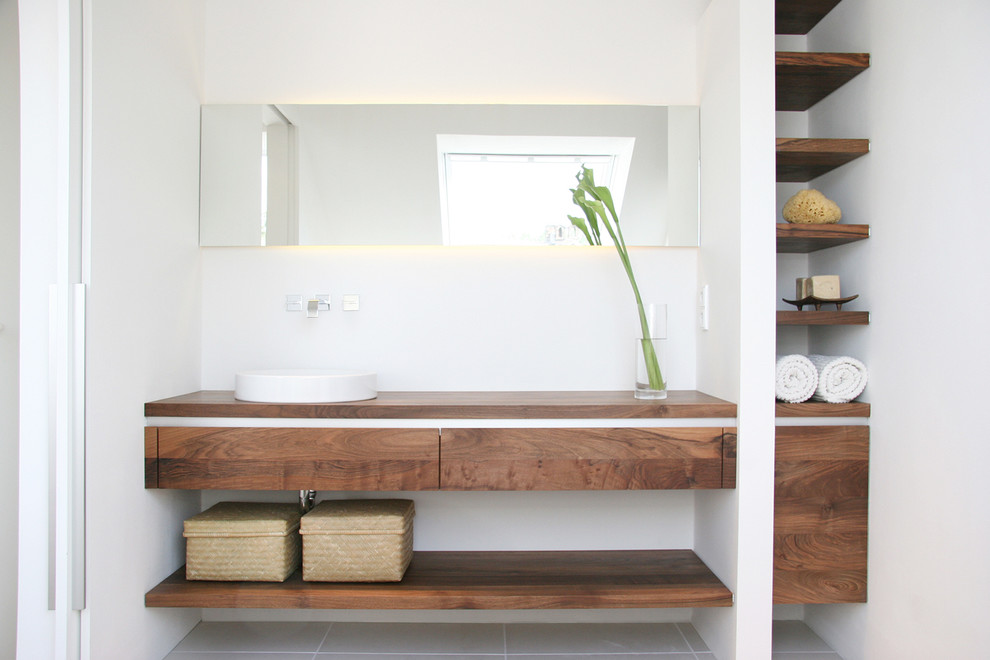 Ispirazione per una stanza da bagno minimal con ante lisce, ante in legno scuro, pareti bianche, lavabo a bacinella e top in legno
