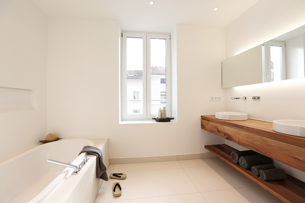 Idée de décoration pour une salle de bain minimaliste en bois foncé de taille moyenne avec un placard à porte plane, une baignoire posée, une douche à l'italienne, WC séparés, un carrelage beige, des carreaux de céramique, un mur blanc, une vasque et un plan de toilette en bois.