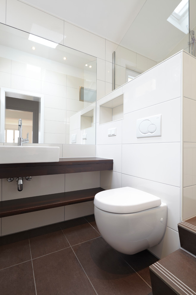 Cette photo montre une petite salle d'eau tendance avec une vasque, un plan de toilette en bois, une baignoire posée, un combiné douche/baignoire, WC séparés, un carrelage blanc et un mur blanc.