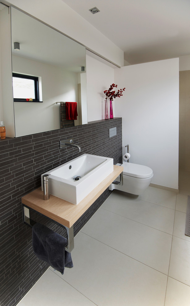 Example of a trendy brown tile and ceramic tile ceramic tile and beige floor bathroom design in Dusseldorf with a wall-mount toilet, white walls, a vessel sink, wood countertops and flat-panel cabinets
