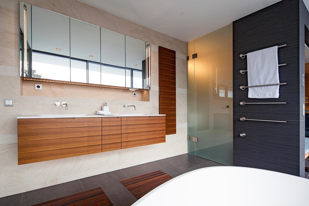 Cette image montre une salle de bain design en bois brun avec un placard à porte plane, une baignoire indépendante, un carrelage beige et des dalles de pierre.