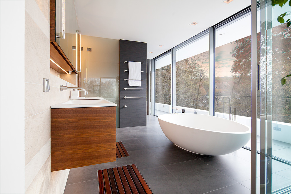 Пример оригинального дизайна: большая ванная комната в современном стиле с плоскими фасадами, фасадами цвета дерева среднего тона, отдельно стоящей ванной, плиткой из листового камня, столешницей из дерева, подвесной раковиной и белой столешницей