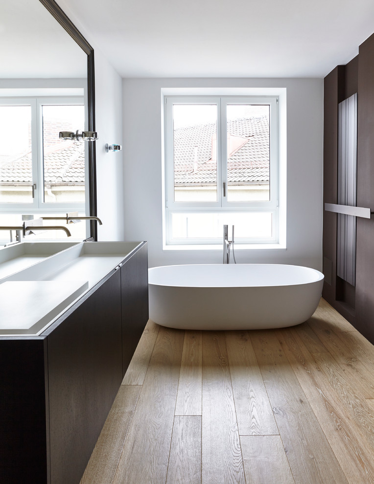 Mid-sized minimalist master light wood floor freestanding bathtub photo in Munich with flat-panel cabinets, dark wood cabinets, white walls, solid surface countertops and a trough sink