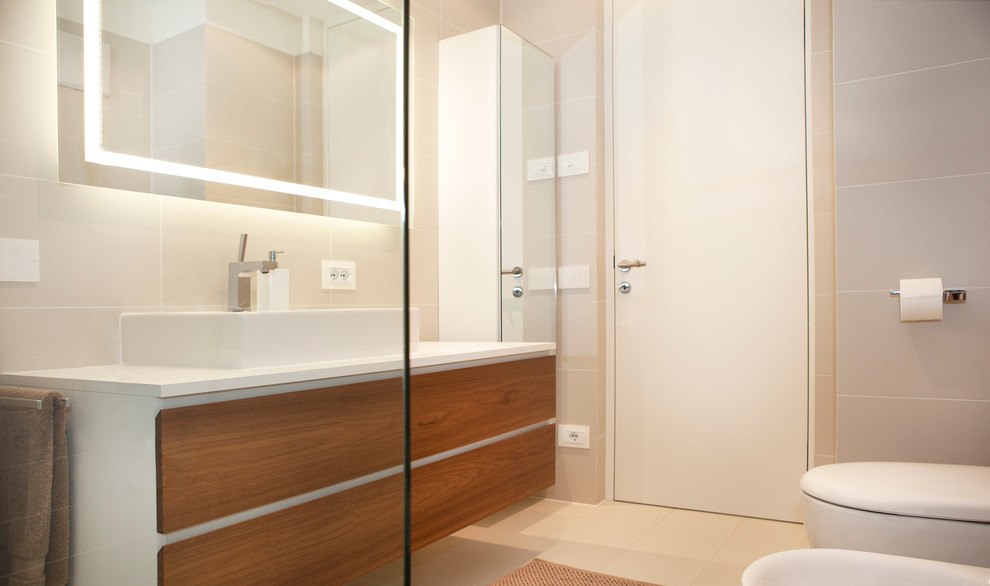 Ejemplo de cuarto de baño actual con armarios con paneles lisos, puertas de armario de madera oscura y baldosas y/o azulejos beige