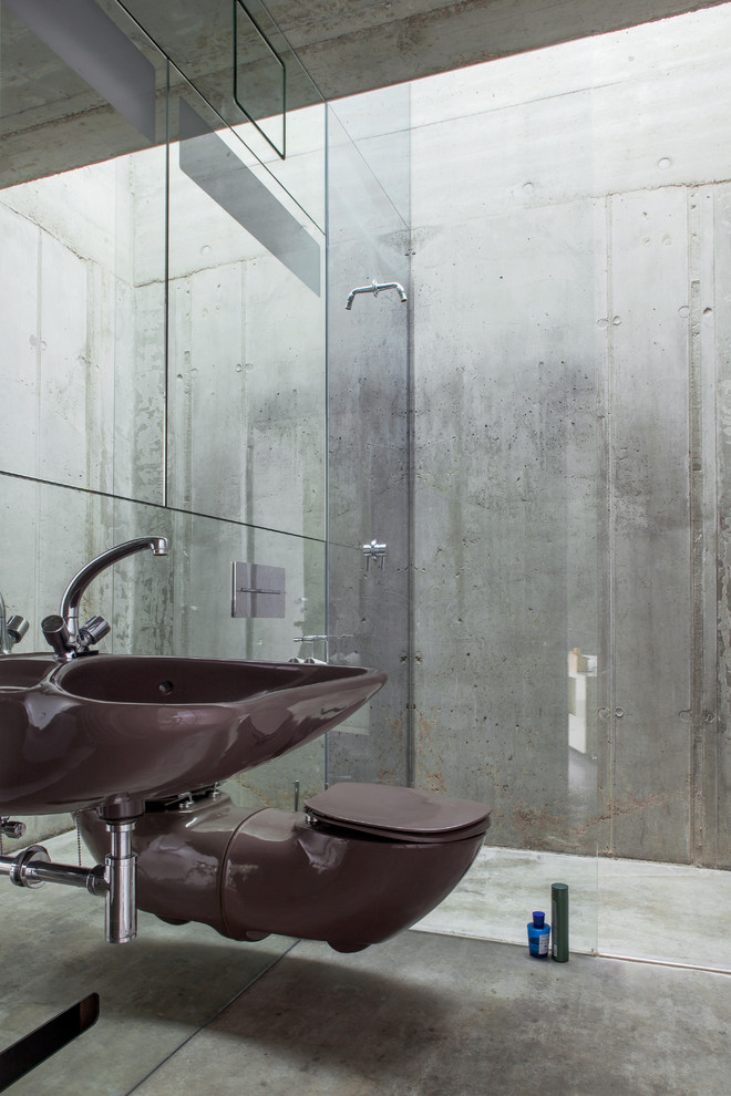 Diseño de cuarto de baño industrial con lavabo suspendido, ducha a ras de suelo, sanitario de pared, paredes grises y suelo de cemento