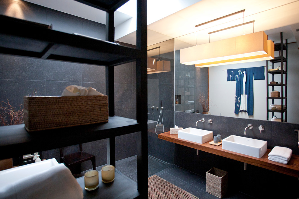 На фото: ванная комната в восточном стиле с инсталляцией, черной плиткой, серыми стенами, настольной раковиной, столешницей из дерева, отдельно стоящей ванной и открытым душем с