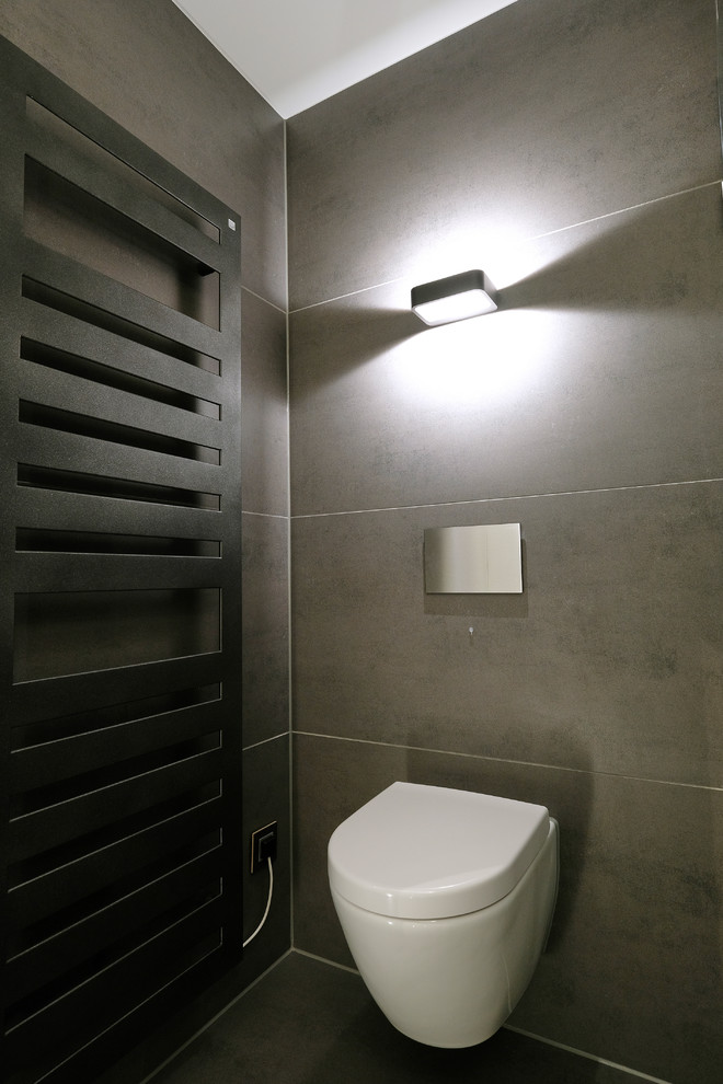 Kleines Modernes Duschbad mit flächenbündigen Schrankfronten, Wandtoilette mit Spülkasten, grauen Fliesen, grauem Boden, schwarzen Schränken, bodengleicher Dusche, grauer Wandfarbe, Unterbauwaschbecken, Schiebetür-Duschabtrennung und schwarzer Waschtischplatte in Dortmund