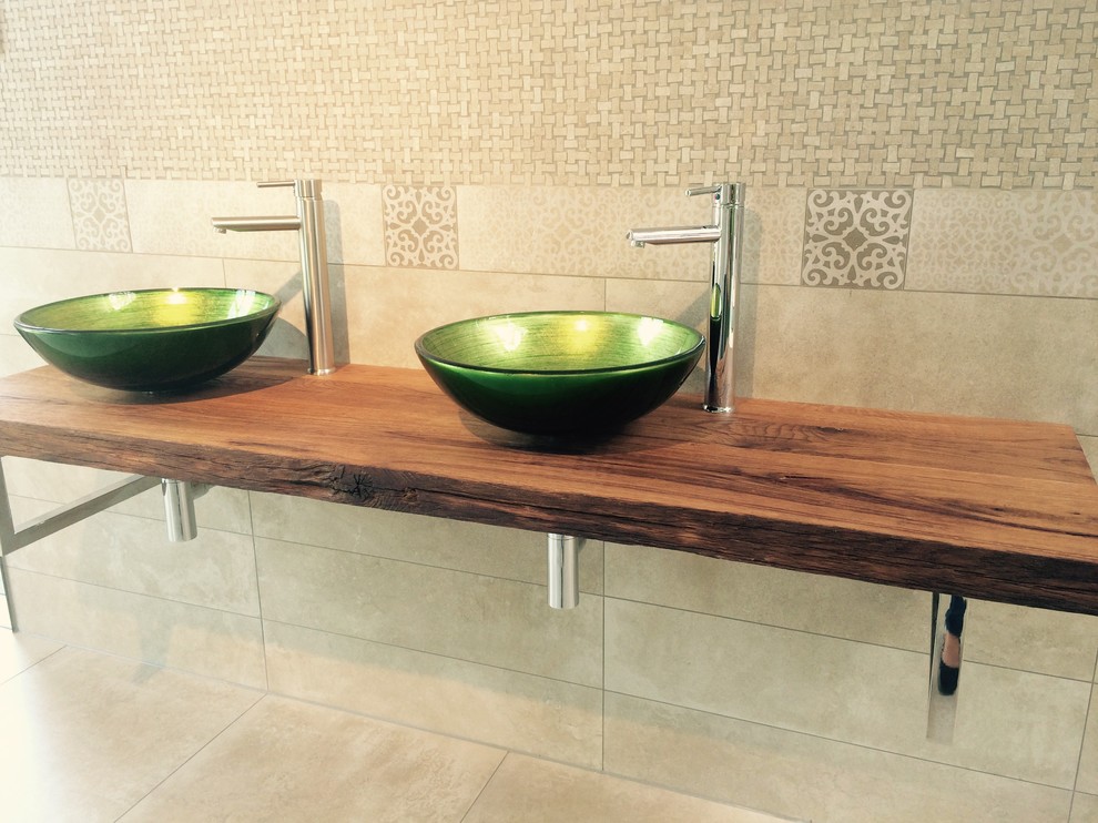 Cette photo montre une salle de bain tendance avec une vasque, un plan de toilette en bois, un carrelage beige, des carreaux de céramique et un sol en carrelage de céramique.