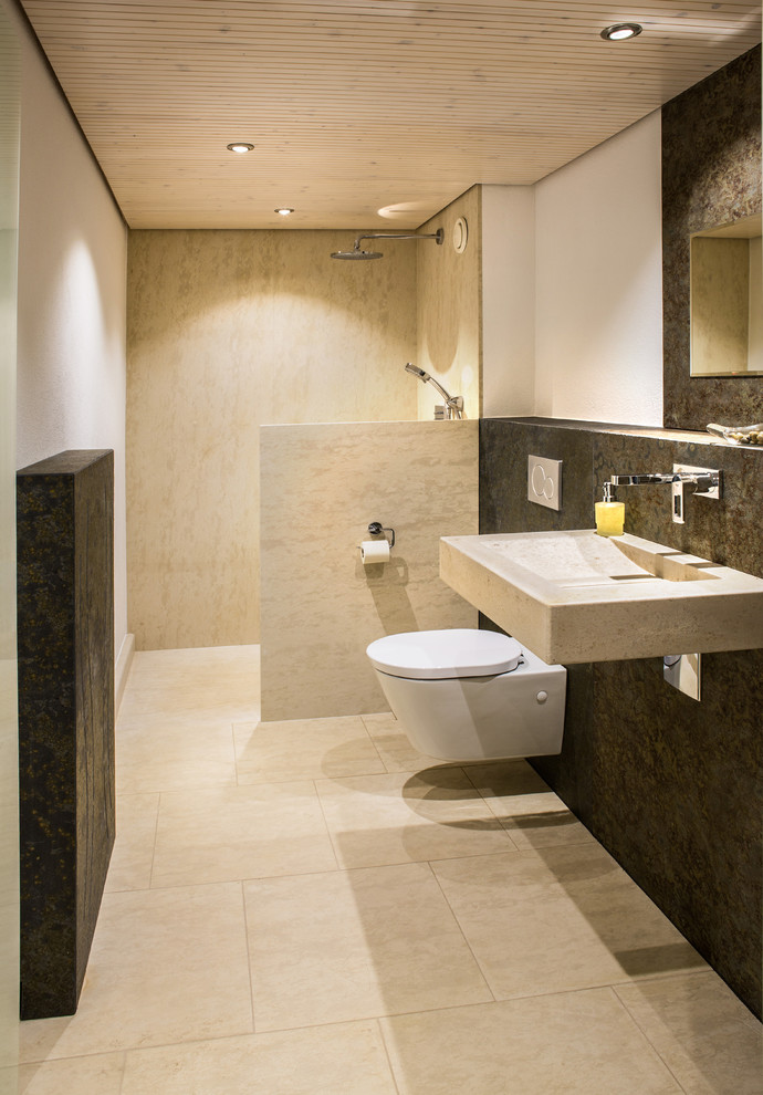 Modern inredning av ett litet badrum med dusch, med en kantlös dusch, en toalettstol med separat cisternkåpa, beige kakel, kakelplattor, gröna väggar, kalkstensgolv, ett väggmonterat handfat, bänkskiva i kalksten, beiget golv och med dusch som är öppen