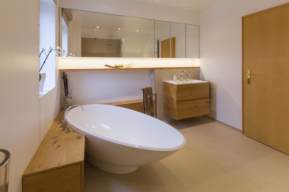 Modelo de cuarto de baño contemporáneo grande con armarios con paneles lisos, puertas de armario de madera oscura, bañera exenta, paredes blancas y lavabo tipo consola