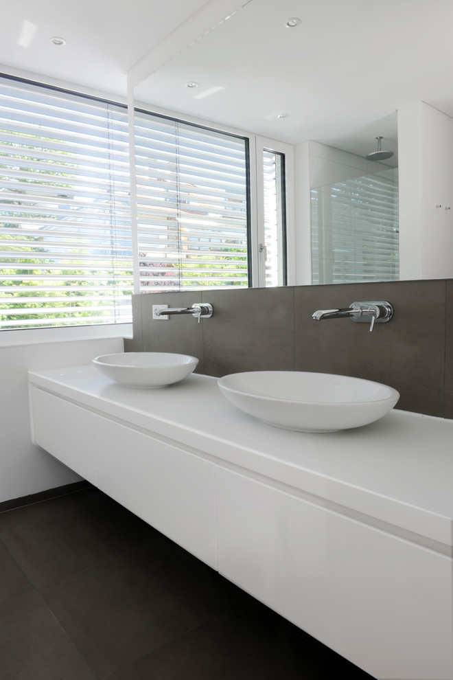 Inspiration pour une salle de bain design de taille moyenne avec un placard à porte plane, des portes de placard blanches, un carrelage gris, un mur blanc, une vasque et un plan de toilette en surface solide.