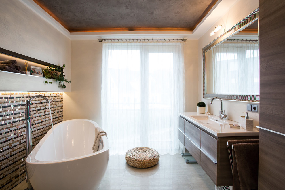 На фото: большая главная ванная комната в современном стиле с монолитной раковиной, плоскими фасадами, отдельно стоящей ванной, разноцветной плиткой, плиткой мозаикой, бежевыми стенами и темными деревянными фасадами с