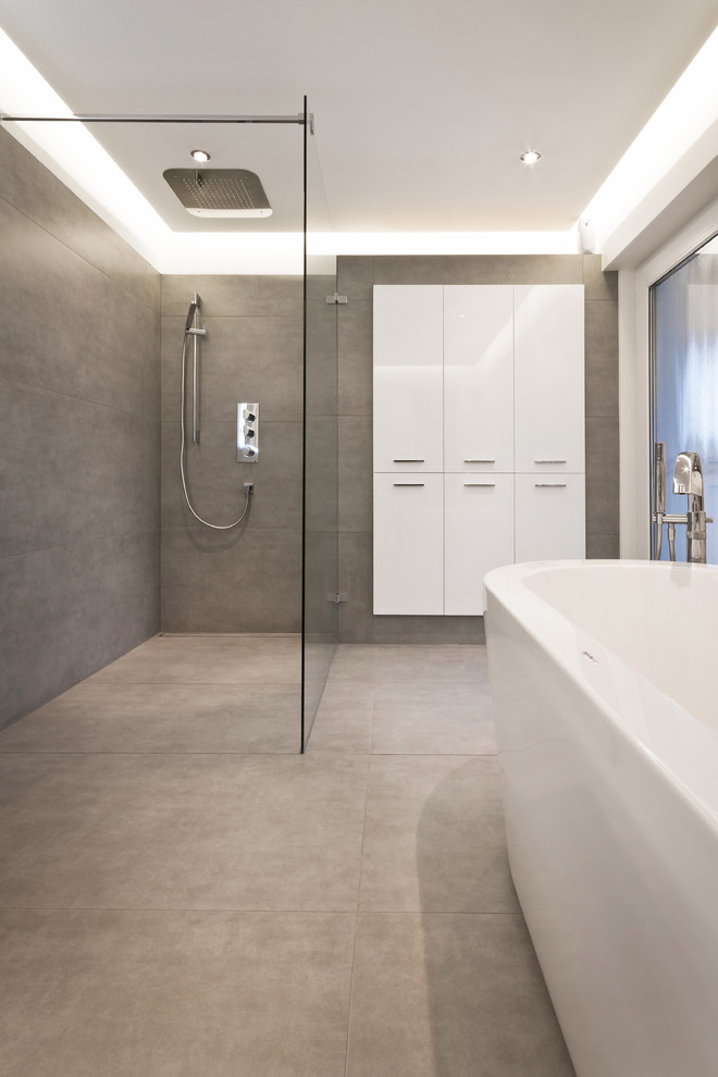 Großes Modernes Badezimmer mit flächenbündigen Schrankfronten, weißen Schränken, freistehender Badewanne, grauen Fliesen, Steinplatten, grauer Wandfarbe und bodengleicher Dusche in Sonstige