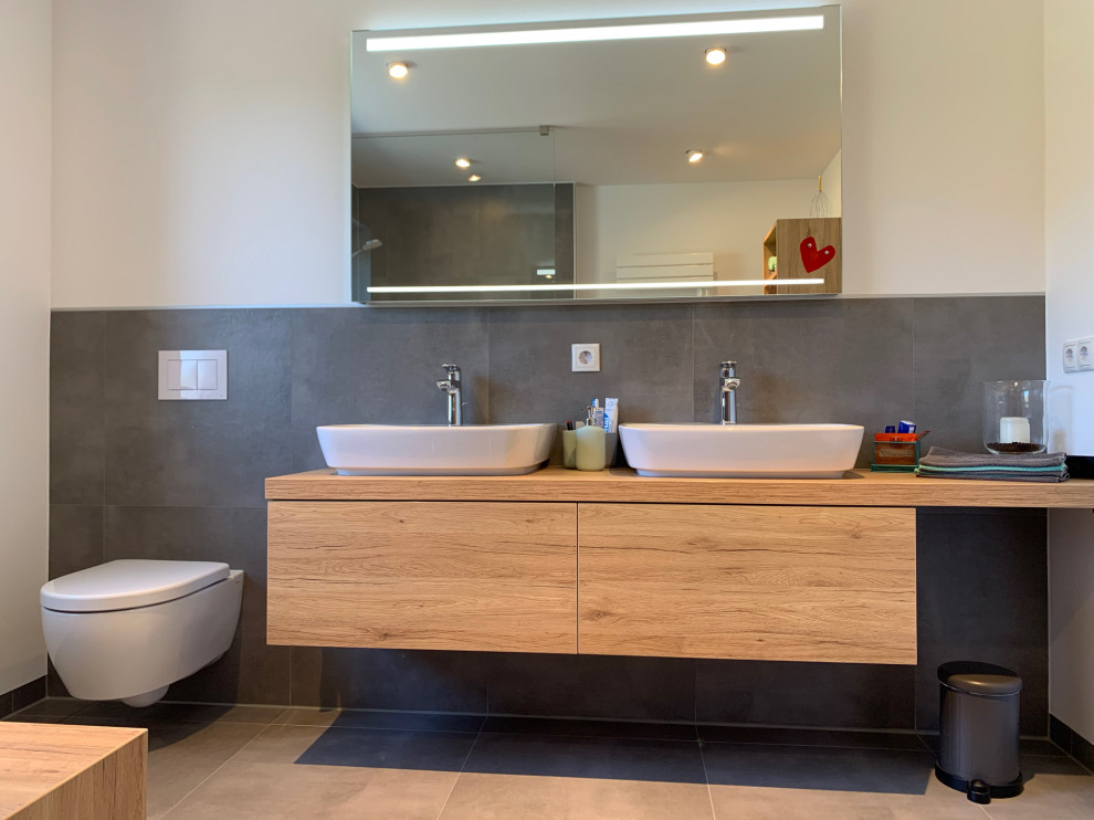 Exempel på ett litet modernt badrum med dusch, med skåp i mellenmörkt trä, en toalettstol med separat cisternkåpa, grå kakel, keramikplattor, vita väggar, klinkergolv i keramik, ett fristående handfat, träbänkskiva, grått golv och med dusch som är öppen