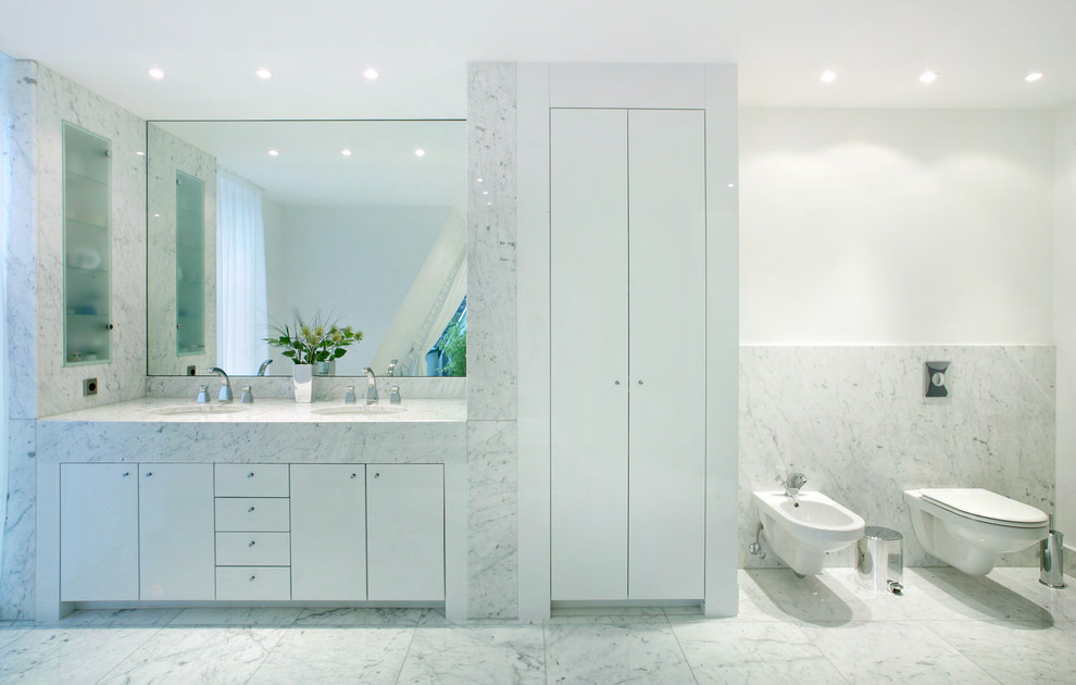 デュッセルドルフにある広いコンテンポラリースタイルのおしゃれな浴室 (アンダーカウンター洗面器、フラットパネル扉のキャビネット、白いキャビネット、白いタイル、白い壁、ビデ、石スラブタイル、大理石の床、大理石の洗面台) の写真