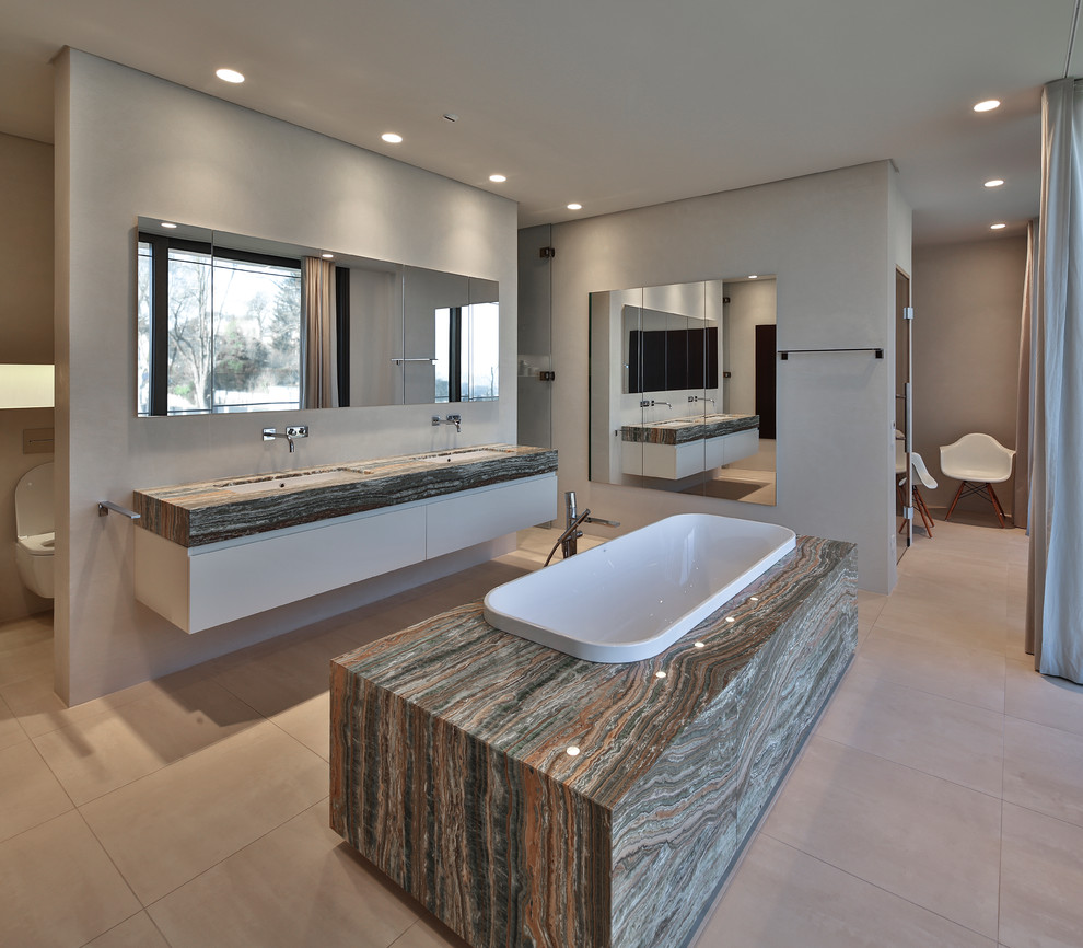 Foto de cuarto de baño actual extra grande con lavabo bajoencimera, puertas de armario blancas, bañera encastrada, paredes grises, armarios con paneles lisos y sanitario de pared